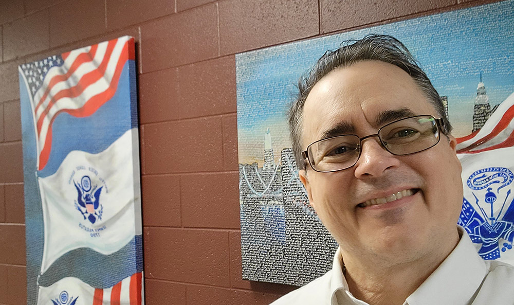 Craig Stevens smiling in front of two paintings hanging on the wall.