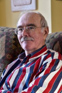 Dr. William Sullivan in his home wearing a red, white, and blue striped button down shirt